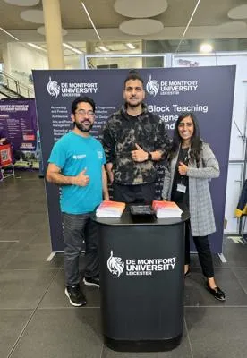DMU staff standing at the DMU stand with banners and materials on display.