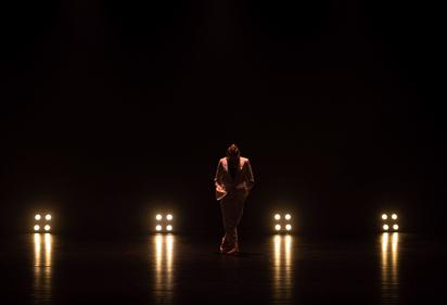 A lone dancer stood on dark stage with isolated spotlights behind them