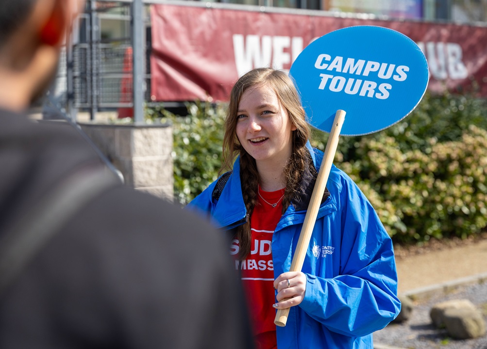 Smiling girl holds up a Campus Tours lollipop whilst talking to a tour group