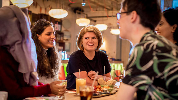Two students in a bright, clean room, looking slightly hesitant about the pizza between them.